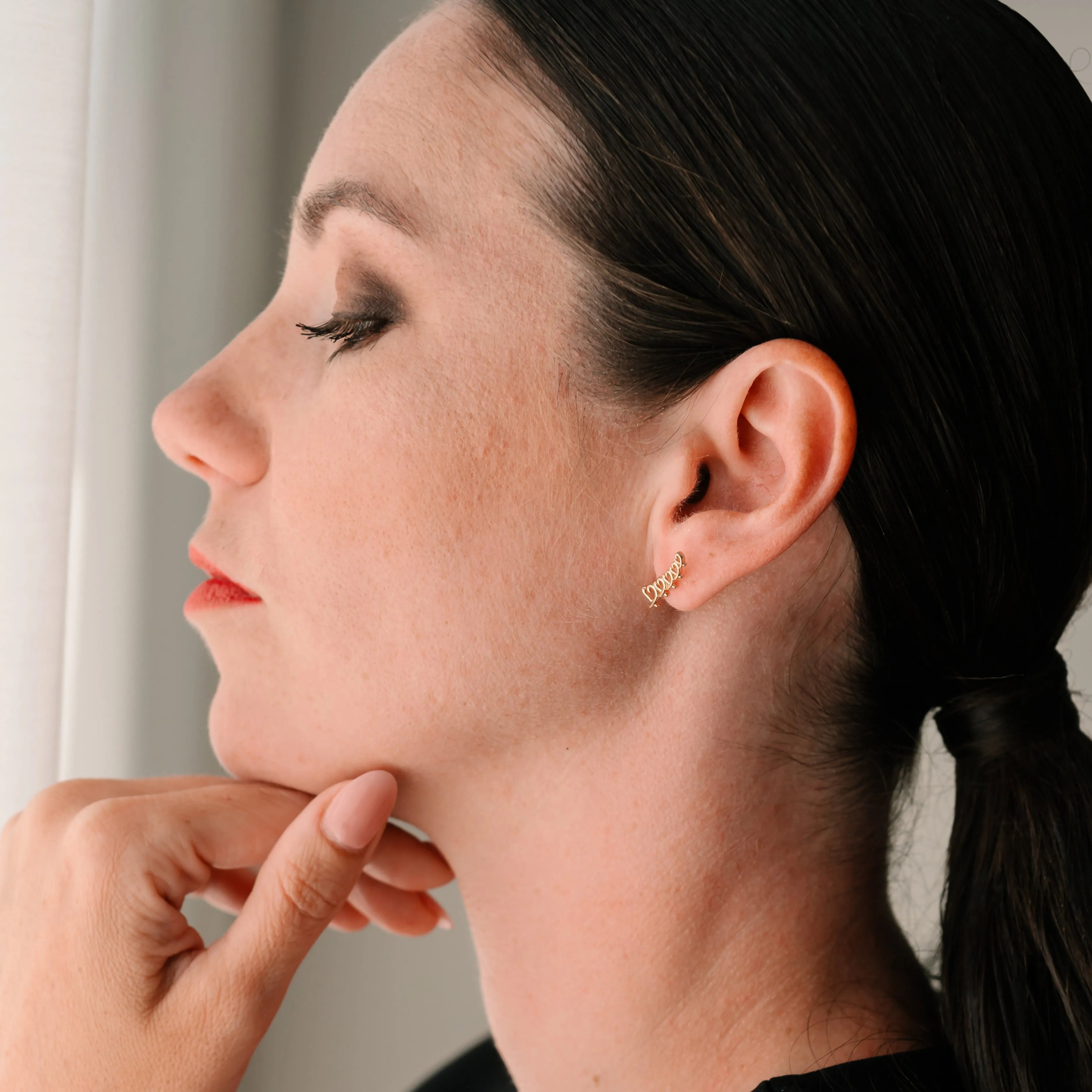 Jemné zlaté náušnice v tvare srdiečok na žene – CREYO Amore